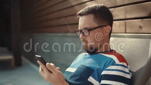 大胡子男人在智能手机屏幕上打字在晴天躺在休息室里视频的预览图