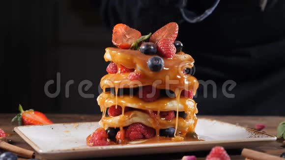 木制桌子上有焦糖和浆果的美味煎饼把红糖倒在煎饼堆上黑色背景视频的预览图