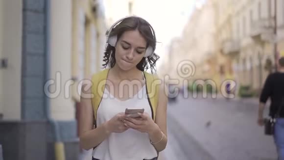 美丽的年轻女子走在城市的街道上听着音乐随之而动享受视频的预览图