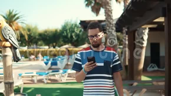 男性游客独自在度假酒店内散步并在手机上观看视频的预览图