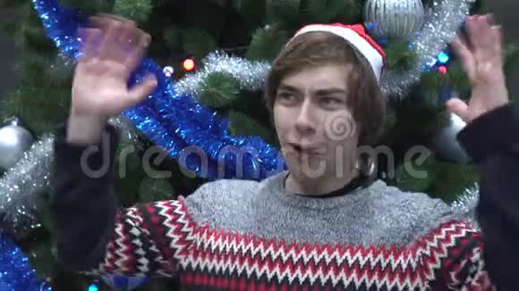 戴着圣诞帽的英俊青年在圣诞树的背景下发出惊喜的尖叫视频的预览图