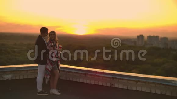 男人和年轻漂亮的女人坐在沙发上拿着酒杯在日落时亲吻屋顶露台视频的预览图