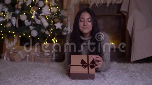 女孩拿着礼物打开盒子高兴地躺在圣诞树附近的地板上4K视频的预览图