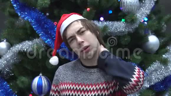 圣诞老人帽中的年轻人肖像圣诞树上脖子上的疼痛视频的预览图