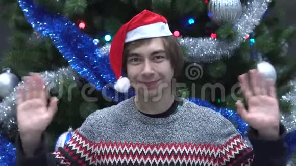 戴着圣诞帽在圣诞树背景上挥舞着手的帅哥视频的预览图