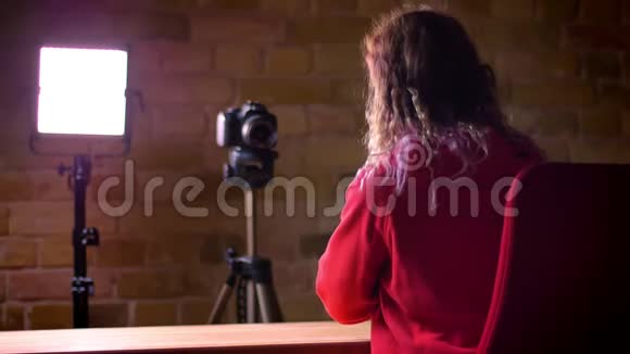 后景年轻博主在红色帽衫录制视频前相机和灯在布里克肯墙背景视频的预览图