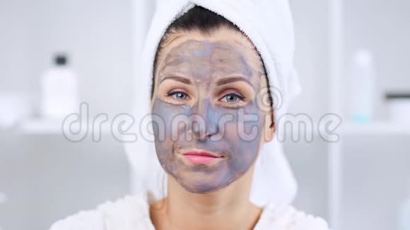 年轻快乐的女人脸上戴着黏土面具看着镜头视频的预览图