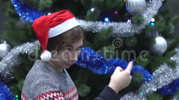 英俊的年轻人戴着圣诞帽邀请别人来圣诞树背景视频的预览图