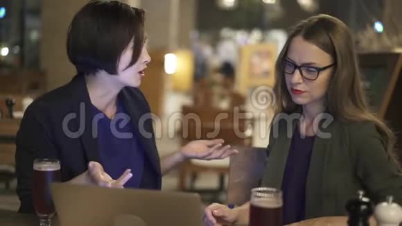 两名年轻女子关闭笔记本电脑晚上在咖啡馆喝啤酒视频的预览图