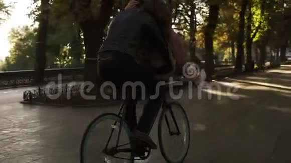 快乐的年轻夫妇骑在同一辆黑色自行车上背景是阳光背光和树木女孩正坐在视频的预览图