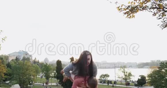 在公园日落时漂亮的年轻女子抱着小女孩快乐的妈妈玩耍拥抱和亲吻她的小女儿视频的预览图