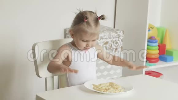 一个小女孩坐在孩子们桌子旁牵着她的手吃意大利面视频的预览图