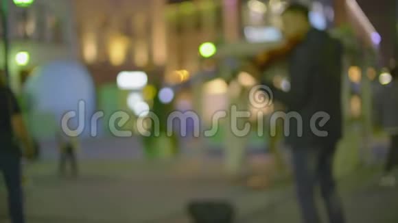 模糊的街头音乐家晚上在灯火通明的步行街拉电小提琴视频的预览图