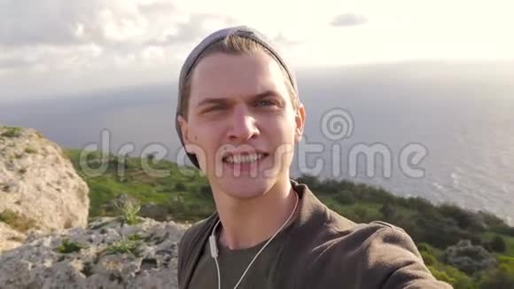 年轻的蓝眼睛家伙在大自然海洋岩石的背景下自拍风日旅游科技满意视频的预览图