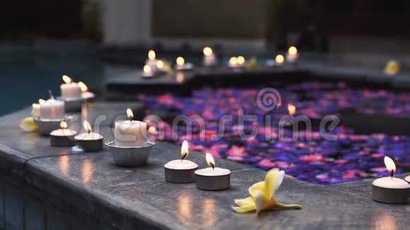 在满是花瓣的游泳池里合上点燃的蜡烛和佛兰吉帕尼的花慢一点的动作视频的预览图