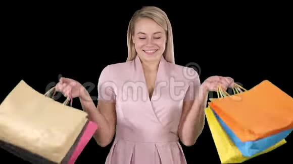 令人兴奋的漂亮年轻女士站在那里看着展示购物袋的摄像机阿尔法频道视频的预览图