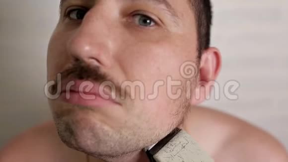一个人用电动剃须刀刮大胡子一个人的特写肖像视频的预览图