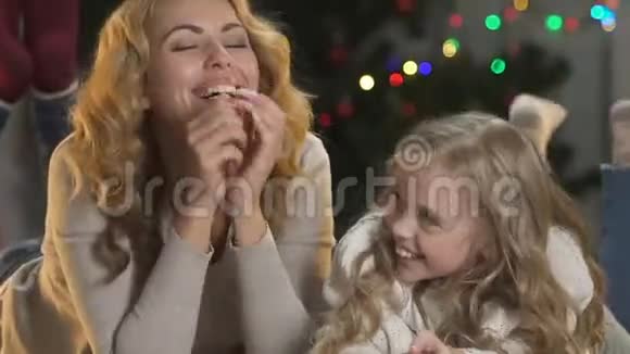 母亲和孩子躺在圣诞树附近双腿颤抖对着镜头微笑庆祝视频的预览图