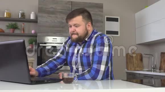 全白种人坐在家里的现代化厨房里在笔记本电脑上工作在家工作网络慢视频的预览图