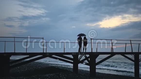 男人和女孩在伞下的剪影在海边享受日落视频的预览图