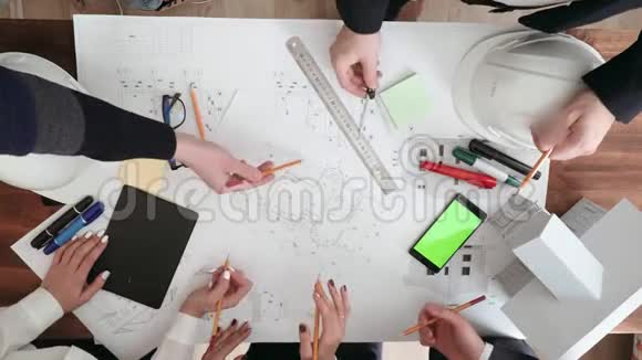 一群人积极地讨论和检查大楼的大图纸桌子上有眼镜记号笔电话视频的预览图
