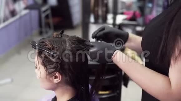 一位造型师用慢镜头拍摄了一位戴手套的女孩将顾客湿漉漉黑发分成几股视频的预览图
