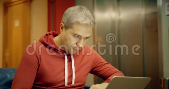 灰发白种人穿着休闲装在酒店走廊里用笔记本电脑视频的预览图