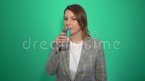 年轻开朗的白种人女人喝着干净的水在绿色的背景上竖起大拇指视频的预览图