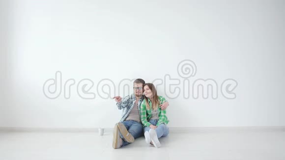 年轻的幸福夫妇正坐在空荡荡的房间里打算在新房子里布置家具视频的预览图