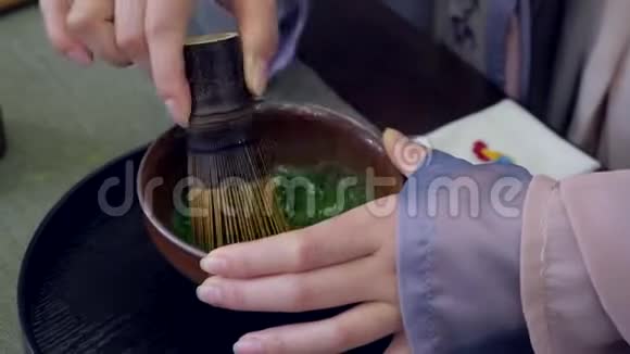 女性手在陶瓷茶碗中搅拌抹茶绿茶粉慢动作视频的预览图