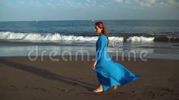 戴着太阳镜和蓝色裙子的女人在黑色的火山海滩上散步视频的预览图