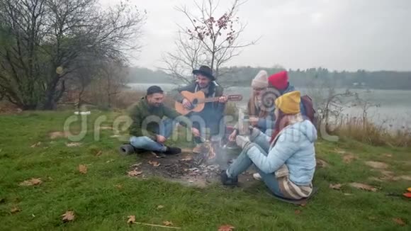 快乐的朋友们坐在沙滩上篝火旁弹吉他唱歌视频的预览图