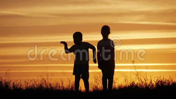 两个孩子在日落时跳舞享受大自然幼儿的剪影快乐的孩子玩得开心享受大自然视频的预览图