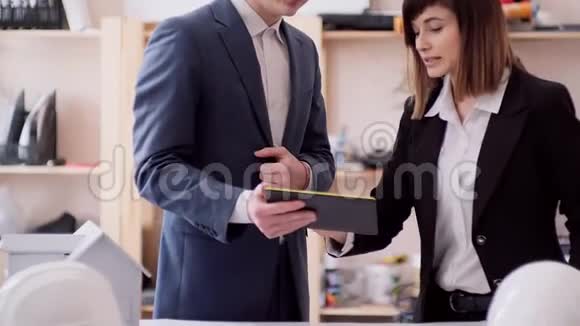 站在桌子旁的棕色头发的女孩在你的平板电脑上解释并展示了工作的时刻视频的预览图