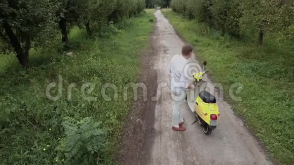 年轻人坐在乡村公路上的滑板车上无人驾驶飞机中弹视频的预览图