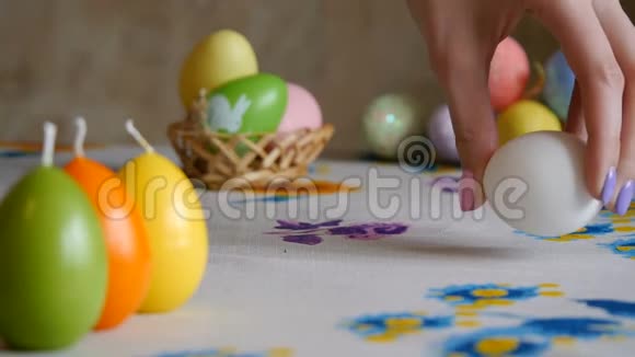 复活节快乐雌性手在桌子上放两个复活节彩蛋五颜六色的蜡烛和五颜六色的复活节彩蛋视频的预览图