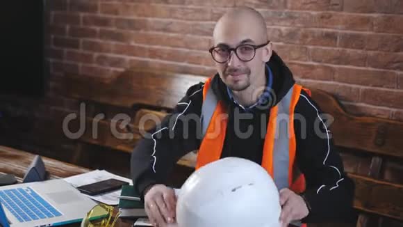 一位男工程师戴着头盔和防护背心在办公桌后面的肖像男人看着相机微笑视频的预览图