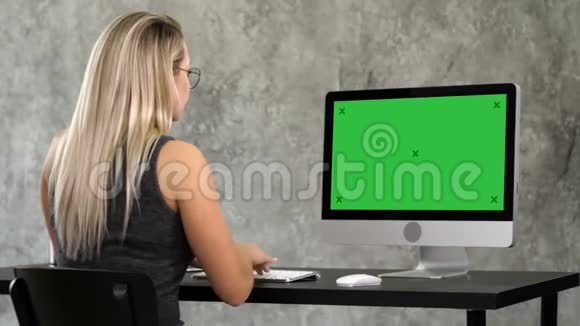 戴着时髦眼镜的时髦女孩坐在电脑前的桌子旁工作绿色屏幕模拟显示视频的预览图