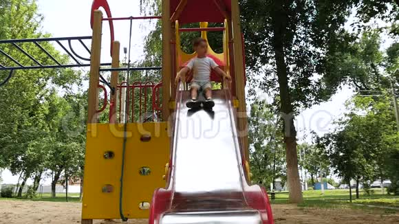 快乐的笑着孩子在操场上玩耍在公园里一个夏天阳光明媚的日子里滚下一张高高的滑梯娱乐视频的预览图