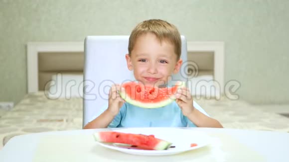 一个可爱的小孩子坐在厨房的桌子旁正吃着一个有食欲的多汁的西瓜浆果水果视频的预览图