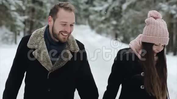 一对年轻迷人的夫妇在大雪下的冬林中散步和玩耍戴粉红帽子的男女拥抱视频的预览图