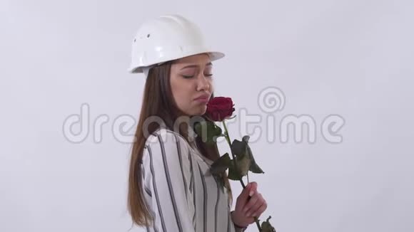 一个戴着白色头盔的快乐美女手里拿着一朵红玫瑰非常快乐地被隔离在白色的背景上视频的预览图