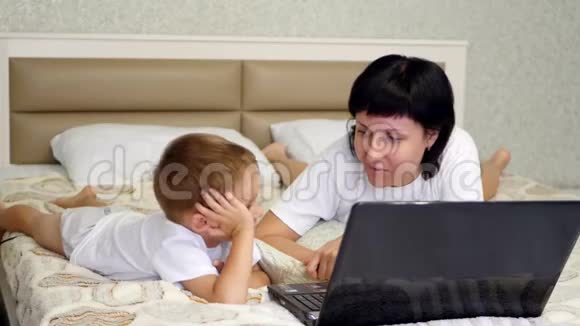 妈妈和宝宝躺在床上正在浏览笔记本电脑上的婴儿装备育儿互联网和视频的预览图