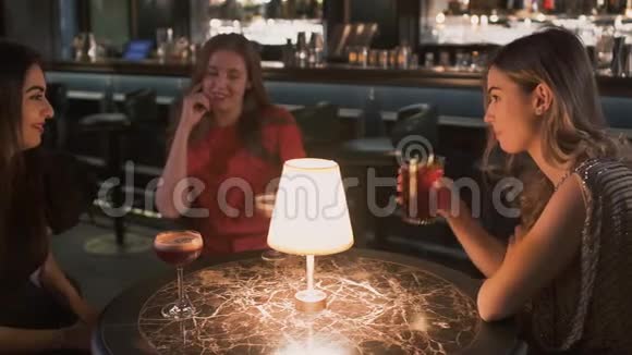 三个快乐的年轻女人坐在酒吧的小桌子旁边女孩们一起庆祝她们聊天视频的预览图