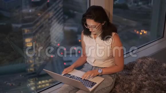 一个年轻的女人用一台笔记本电脑舒适地坐在高处的窗边视频的预览图