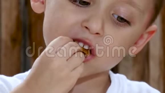 一个孩子坐在木墙背景下的桌子旁吃薯条嘴宝宝特写视频的预览图