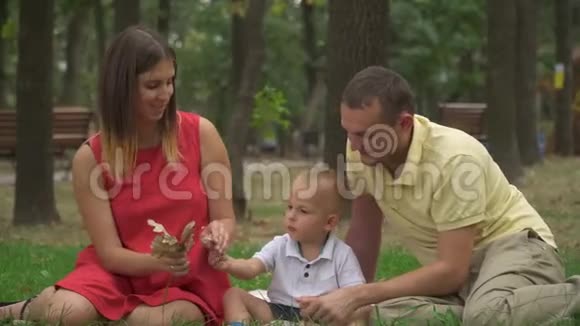 年轻的父母带着他们的小儿子在公园里收集树叶视频的预览图