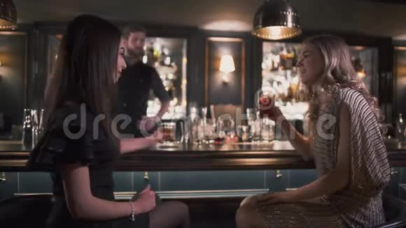 两个女朋友坐在酒吧柜台附近进行有趣的谈话女人喝鸡尾酒休闲视频的预览图