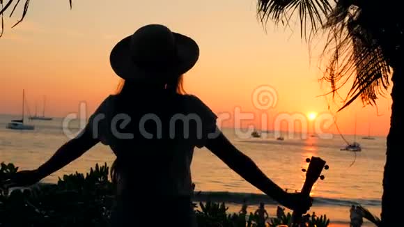 快乐的旅游女孩与乌库勒吉他站在美丽的热带海滩日落伸展的手臂4K泰国视频的预览图