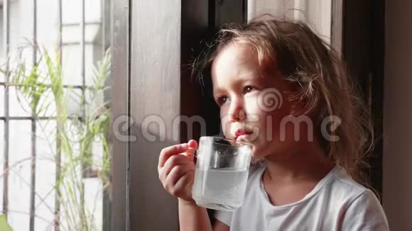 小可爱的女孩正在喝她的饮料看着窗户视频的预览图